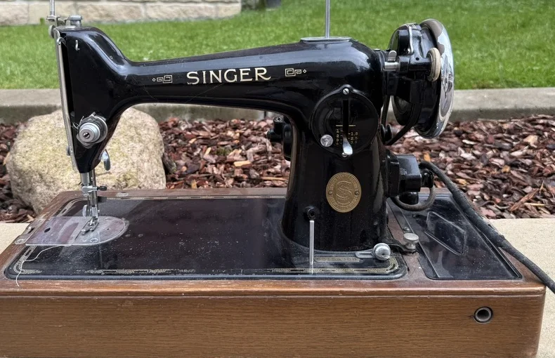 A vintage black Singer sewing machine with gold decals on a wooden base.